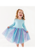 A young girl with curly blonde hair is smiling and laughing while twirling, wearing a light blue long-sleeve top and a voluminous tulle tutu skirt with a blue, purple, and pink gradient and glittery speckles. She is posing on a clean white studio background. Bird and Bean Dresses