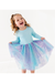 A young girl with curly hair wearing a light blue long-sleeve top and a sparkly blue, purple, and pink tulle tutu skirt, smiling and twirling against a bright white background. Bird and Bean Kids