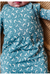 A close-up of a baby wearing a long-sleeve bamboo sleep sack in dusty blue with a white crescent moon and star pattern, lying on a textured brown blanket. Bird and Bean Baby Gifts 