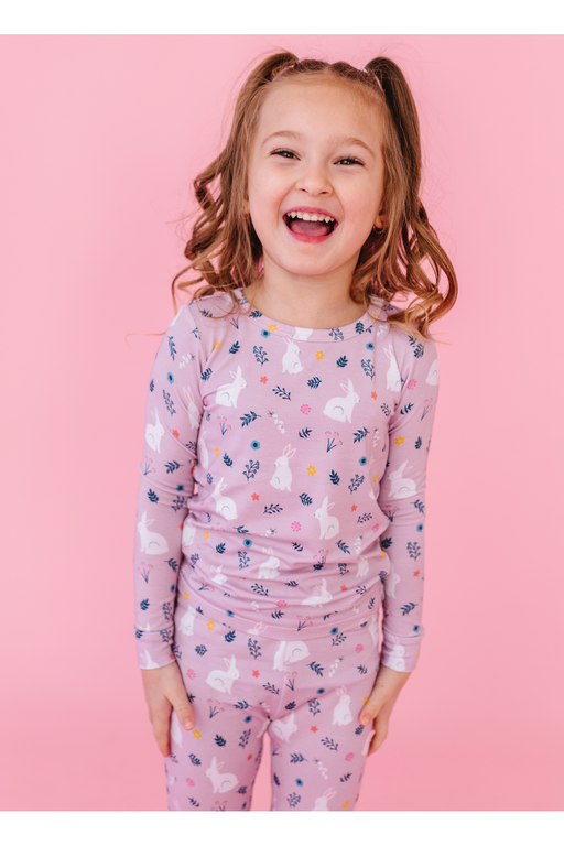 Young girl wearing a pink pajama set with animal prints against a pink background -Bird and Bean Kids