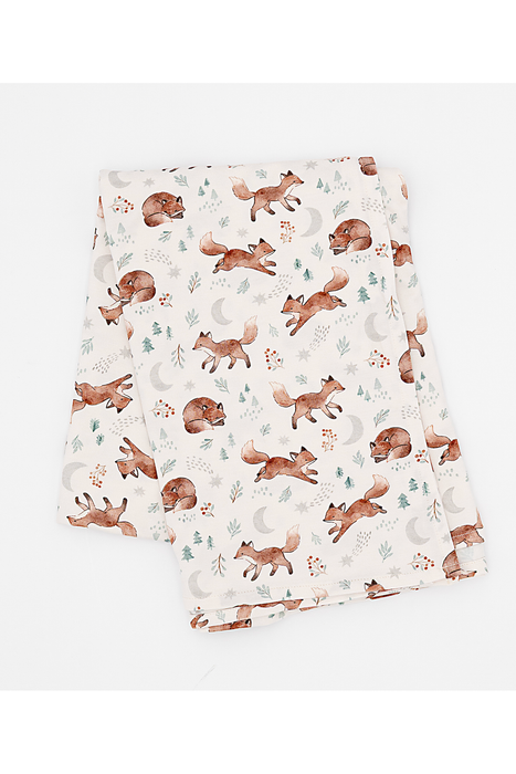 A folded fabric swaddle, featuring a watercolor-style print of brown foxes, crescent moons, pine trees, and small floral motifs on a warm cream background. Bird and Bean Baby 
