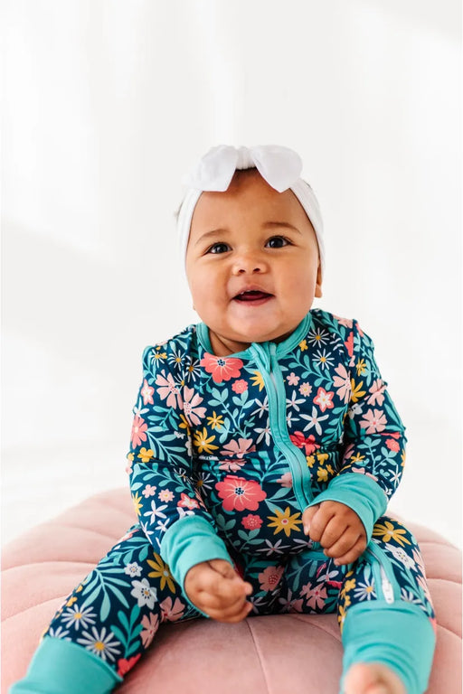 Smiling baby model in Maren Floral One Piece Zip Sleep Romper with pink flowers on navy background. 