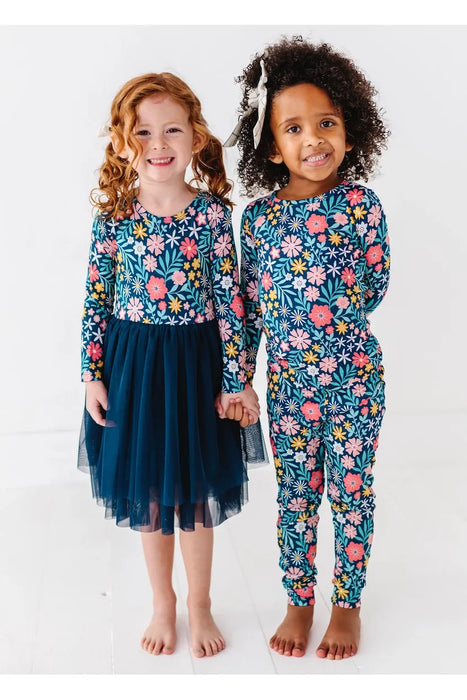 Two child models, one in Bamboo Maren Peach, gold, and pink flower navy pajama set and one in matching Bamboo Maren Navy Tulle dress
